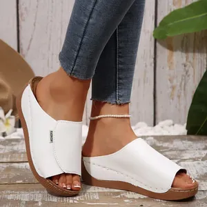 Close-up of white wedge mule sandals with stitched details and brown rubber sole