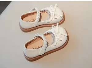 Detalle de elegantes zapatos de princesa blancos para niña con perlas, lazo y adornos de encaje.