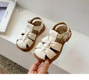 Close-up of girls cream closed-toe sandals with bow detail and adjustable buckled strap
