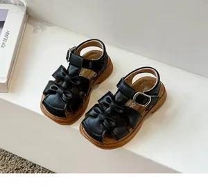 Detail view of black girls closed-toe sandals with bow accents and soft brown soles