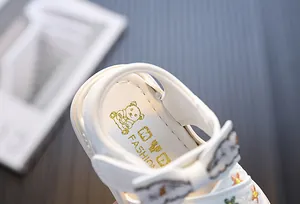 Detailweergave van witte peutersandalen met bloemborduursel en goudkleurig logo