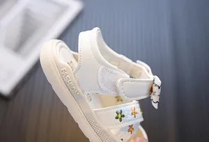 Close-up van witte sandalen voor meisjes met bloemenborduurwerk en strikdetail.
