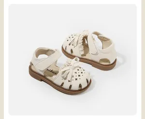 Detail shot of cream girl's toddler sandals with bow and lace trim on white background.