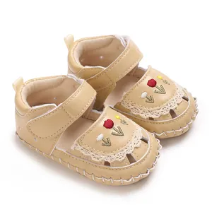 Dettaglio di sandali beige per neonata con fiori ricamati e finiture in pizzo eleganti
