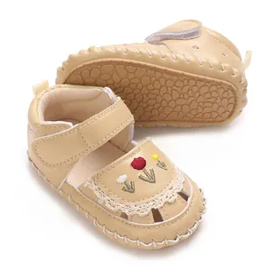 Dettaglio ravvicinato di sandali beige per neonati con ricami floreali e pizzo.