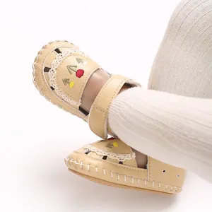 Dettaglio ravvicinato di sandali beige per neonati con ricamo di alberi e pizzo morbido.