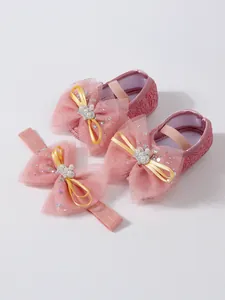 Vue détaillée de chaussures de bébé rose en dentelle avec un bandeau rose assorti