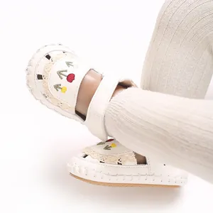 Dettaglio di sandali bianchi per neonata con ricami floreali colorati e pizzo decorativo