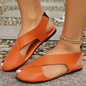 Modische orangefarbene geschlossene Römersandalen mit Kreuzriemen auf einem Gehweg