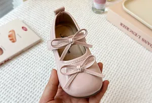 Close-up detail of pink patent leather Mary Jane shoes featuring delicate double bow accents