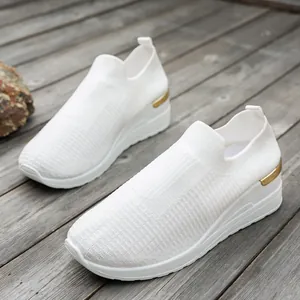 Detailed side view of white fly-knit wedge sneakers for women on a wood background