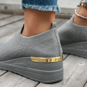 Detailed close-up view of gray fly-knit wedge sneakers featuring a stylish metallic gold heel accent