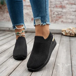 Close-up of black breathable fly-knit slip-on sneakers for women on a wooden deck.