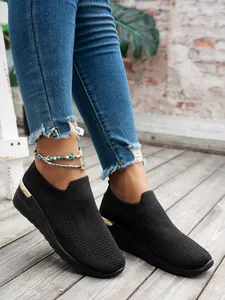 Detailed view of women's black knit wedge sneakers with breathable mesh and gold heel accent.