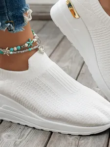 Close-up of flyknit texture on white slip-on wedge sneakers for women on wooden deck.