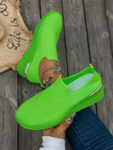 Close-up detail of neon green fly-knit platform wedge sneakers with metallic heel accent