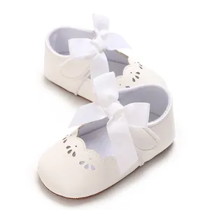 Vista detallada de zapatos de princesa para bebé blancos con gran lazo y calados