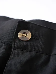 Nahaufnahme eines braunen Schildpattknopfs am Taillendetail einer schwarzen Herrenhose