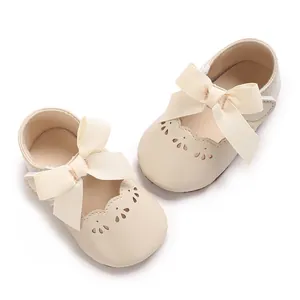 Detalle de zapatos beige de princesa para bebé con lazo grande y calados ondulados