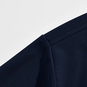 Gros plan sur le tissu piqué respirant bleu marine et la couture d'épaule d'un polo homme.