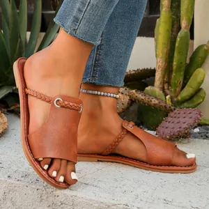 Close-up of tan leather flat sandals with braided straps in an outdoor setting.