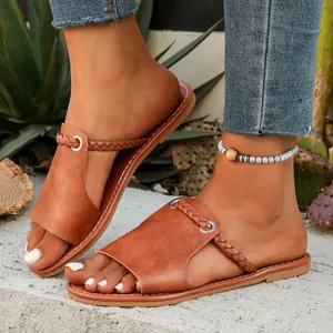 Detail view of women's flat sandals featuring braided straps and tan faux leather.