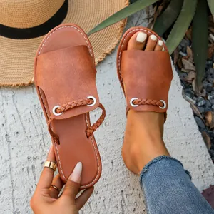 Close-up of brown flat sandals with braided strap and white stitching on the foot.