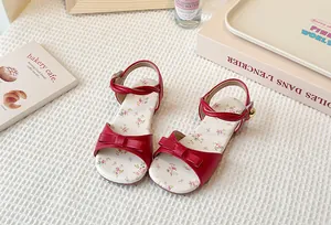High-angle detail of red girls' sandals with bow and floral print insoles.
