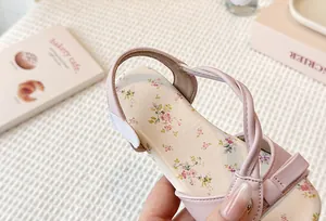 Detail shot of pink girls floral flat sandals with bow and criss-cross straps.
