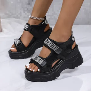 Détail de sandales à plateforme noires avec strass et brides velcro portées par un mannequin