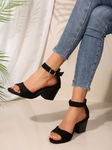 Nahaufnahme der schwarzen Sandalen mit Knöchelriemen und Blockabsatz zu einer Jeanshose