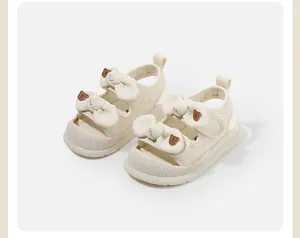 Dettaglio di sandali color crema per bambina con fiocchi eleganti e piccoli orsi