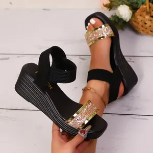 Detailaufnahme der schwarzen Keilsandalen mit glitzerndem Goldriemen und Gummiband