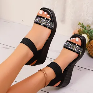 Nahaufnahme von schwarzen Plateau-Keilsandalen mit Glitzerriemen und Gummiband