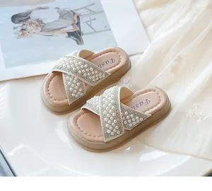 Primer plano de los detalles de perlas y strass en las sandalias cruzadas beige de niña.