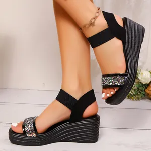 Detailansicht der schwarzen Keilsandalen mit elastischen Riemen und Glitzerbändern.
