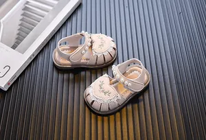 Close-up of baby girl sandals with pearl strap and floral heart embroidery detail.