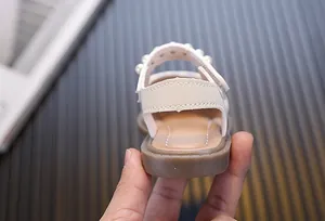 Detail of cream baby girl sandals with pearl strap and soft brown sole
