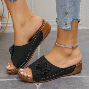 Gros plan de sandales compensées noires pour femmes avec fleur décorative et perforations.