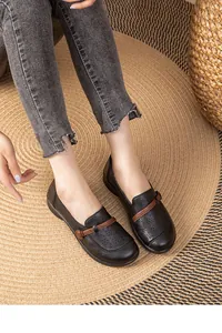 Close-up view of black breathable hollow leather loafers worn on a woven straw rug