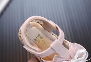 Detailed macro view of pink toddler sandals featuring an elegant pearl bow and soft insole