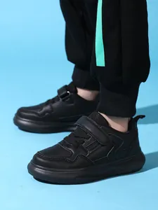 Détail de baskets en cuir noir pour enfants avec semelles épaisses et bandes velcro.