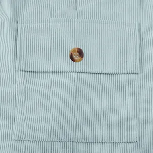 Detail of a buttoned flap pocket on men's light blue corduroy cargo shorts texture view.