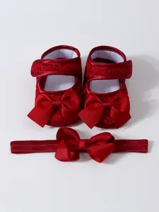 Nahaufnahme roter Spitzen-Babyschuhe mit großen Schleifen und passendem Stirnband