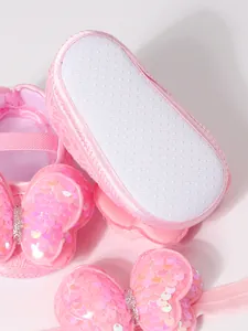 Detalle de zapatos rosa para bebé con suela antideslizante y lazo de mariposa con lentejuelas