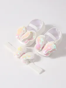 Primer plano de zapatos de bebé de encaje blanco y diadema con alas de mariposa de lentejuelas