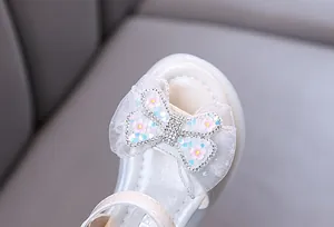 Close-up detail of decorative lace bow with sparkling rhinestones on girl's white sandal