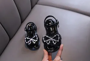 Detailansicht von schwarzen Mädchen-Sandalen aus Lackleder mit glitzernder Schleife