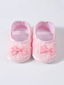 Close-up of pink infant princess shoes with delicate lace and satin bow details