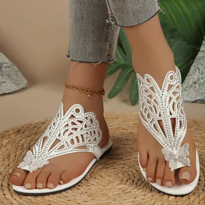 Detailed view of white flat sandals featuring sparkling rhinestones and a butterfly accent.